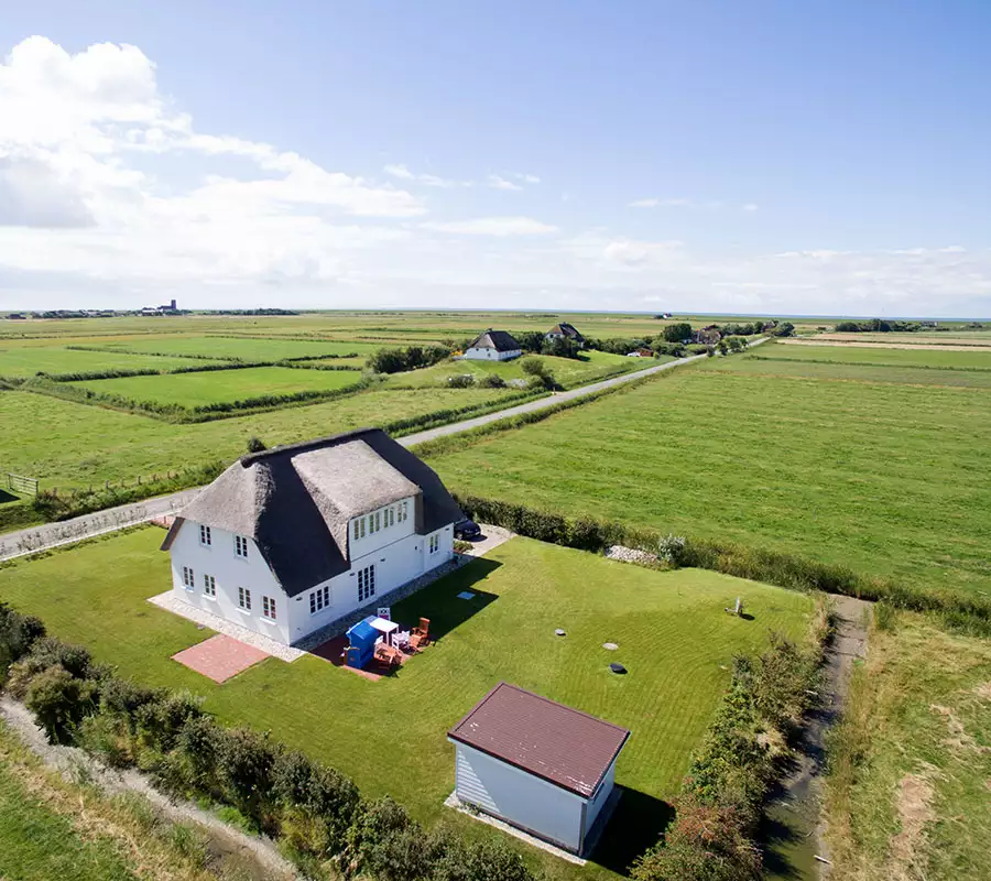 Luftaufnahme eines reetgedeckten Ferienhauses mit großem Garten inmitten grüner Marschwiesen an der Nordsee – Ferienhausfotografie von Ines Preißer