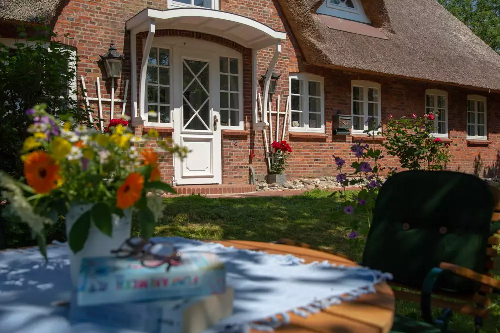 Friesisches Reetdachhaus aus rotem Klinker auf Pellworm mit Blumenstrauß auf dem Gartentisch – Ferienhausfotografie