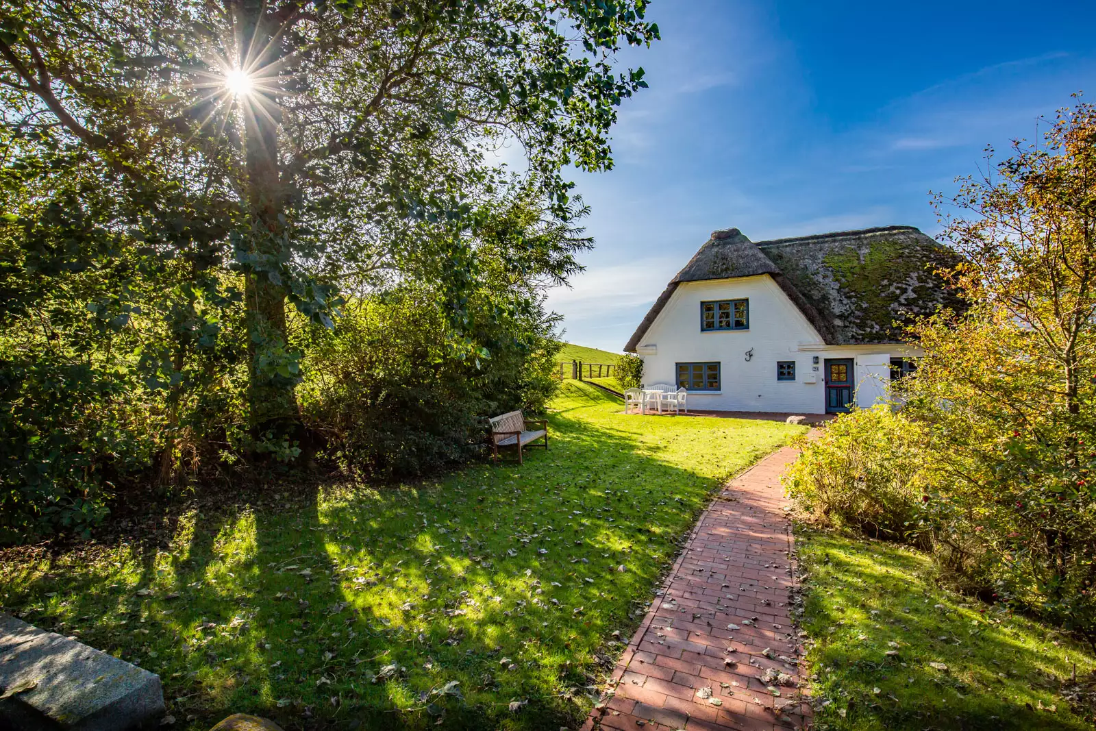 Reetgedecktes Friesenhaus auf Pellworm mit Garten und Klinkerweg im Sonnenlicht – Ferienhausfotografie