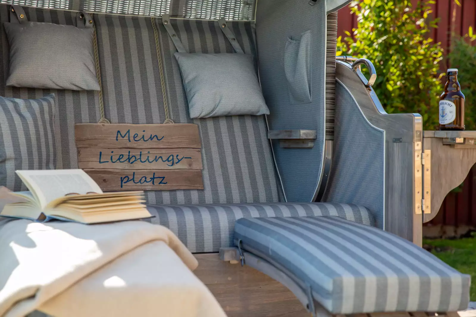 Strandkorb mit Kissen, Buch und Schild „Mein Lieblingsplatz“ im Garten eines Ferienhauses auf Föhr