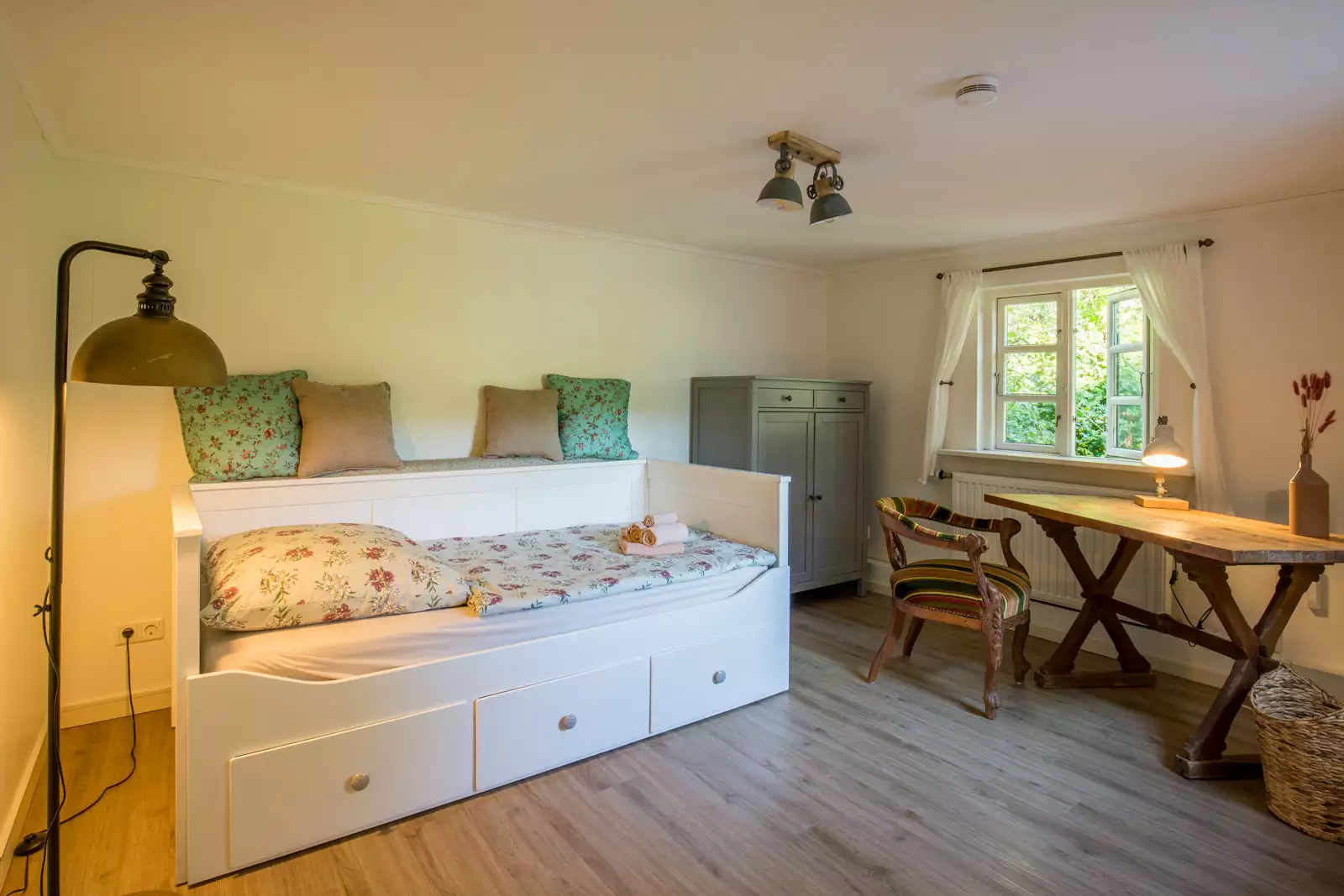 Gästezimmer mit weißem Tagesbett, Holzschreibtisch und Blick ins Grüne in einem Ferienhaus auf Pellworm