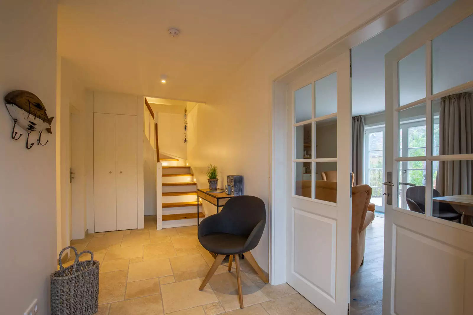 Eingangsbereich mit Natursteinboden, Treppe und Sprossentüren zum Wohnzimmer in einer Ferienunterkunft auf Föhr