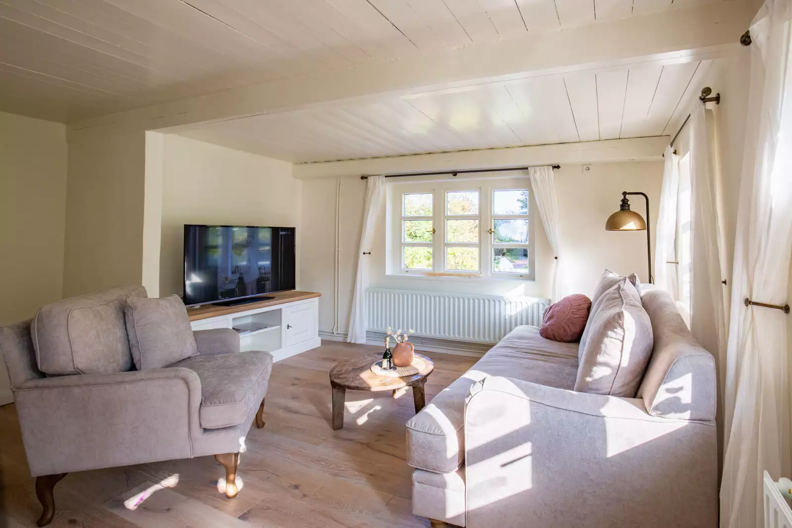 Lichtdurchflutetes Wohnzimmer mit Sofa, Sessel und weißer Holzdecke in einem Ferienhaus auf Pellworm – Ferienhausfotografie